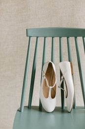 White leather ballerina flats with a round toe shape and a low heel. The flats have a simple, minimalist design and are suitable for casual or formal wear.