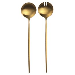 A set of two golden salad servers, including a spoon and a fork, on a dark plate.