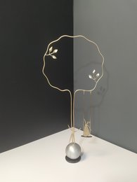 Elegant metal sculpture with abstract floral design and hanging pearl accent. Minimalist, modern style.