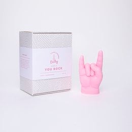 A pink, rock-shaped candle in a white box with a graphic design. The candle is in the shape of a hand making the "rock on" hand gesture, in a vibrant pink color.