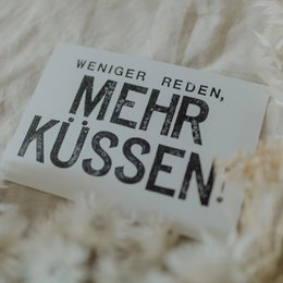 Stamped postcard with German text "mehr kuessen" (more kissing) on a textured background.