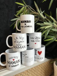 Ceramic mugs with text and graphics celebrating mothers, including phrases like "La vie est si jolie avec maman" (Life is so pretty with mom) and "Maman trop géniale" (Mom is too awesome). The mugs feature a variety of designs and messages honoring mothers.