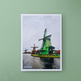 Postcard featuring a scenic view of traditional Dutch windmills on the water, with a green windmill as the focal point.