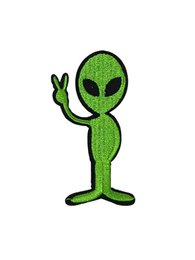Green alien brooch with peace sign hand gesture. Unique and quirky design featuring an extraterrestrial figure in a vibrant green color with a black outline. This brooch would make a fun and eye-catching accessory for any outfit.