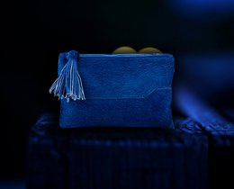 A blue suede clutch bag with a tassel detail, suitable for formal or casual occasions.