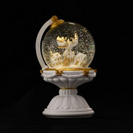 A white, globe-shaped Christmas snow globe with an automatic snowstorm and lights. The snow globe features a winter scene with deer inside.