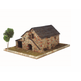 A traditional Spanish stone house with a tiled roof, surrounded by a small garden or yard. The house has a rustic, historic appearance with stone walls and a charming architectural style.