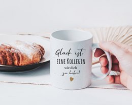  A white ceramic mug with the text "Endlich Schulkind" (Finally a school child) and colorful polka dot patterns. The mug is being held by a person's hands against a striped background.