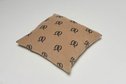 Cushion cover with a repeating pattern of the letter "R" in black on a beige background. The cushion cover has a square shape and appears to be made of a soft, textured fabric.