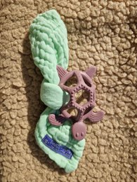 A soft, textured teether in the shape of a turtle with a purple and green color scheme. The teether features a variety of textures and shapes to stimulate a baby's senses during the teething process.