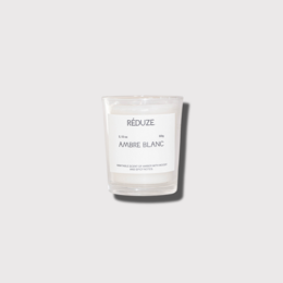 A small, white, round candle with a simple label that reads "Ambre Blanc - Kleine Kerze". The candle appears to be a scented candle, likely with an amber or white fragrance.