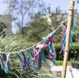 Colorful tassel garland with shades of khaki, blue, pink, and off-white. Decorative party bunting made of fabric tassels hanging on a clothesline in an outdoor setting.