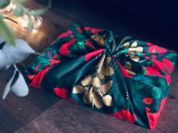 Luxury satin wrapping paper with a floral pattern featuring red, green, and white flowers. The design has a nature-inspired, artistic style.