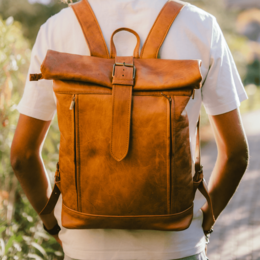 Handcrafted goat leather explorer backpack in black, brown, and natural colors. Features a roll-top design and adjustable straps for a comfortable, unisex fit.