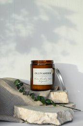 Tall, round white candle with a golden label featuring the text "Scented candle n°13 White flowers Topaz Bergamot". The candle is surrounded by natural stones and greenery, creating a serene and natural atmosphere.