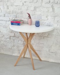 A round, white table with wooden legs and a variety of items on top, including a red box, a blue glass, and other decorative elements. The table is surrounded by two black chairs.