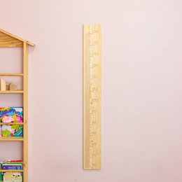 A wooden growth chart ruler with markings for measuring a child's height. The ruler is made of light-colored wood and has clear markings in both centimeters and inches.