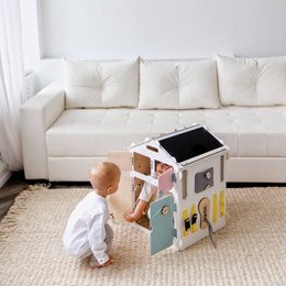 A wooden toy set with a little house and a creative cube. The set includes pastel colors and features a busy board design.