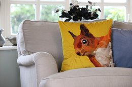 A vibrant, artistic cushion featuring a close-up portrait of a red squirrel against a bold yellow background. The cushion has a plush velvet texture and would make a stylish addition to any living space.