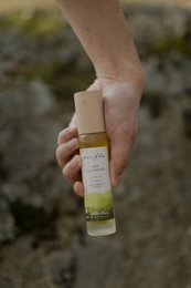 A natural 3-in-1 face oil cleanser, hair oil, and face oil in a glass bottle held in a hand.