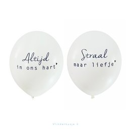 Two white balloons with handwritten text in Dutch, one saying "Altijd in ons hart" (Always in our hearts) and the other saying "Straal maar liefje" (Shine, my dear). The balloons are displayed on a wooden surface along with other decorative items.