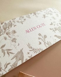 Floral patterned postcard with "All's well" text, enclosed in a pink envelope with a ribbon.