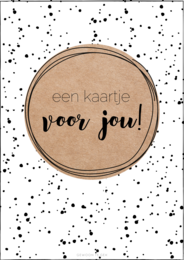 A kraft-colored card with the text "een kaartje voor jou!" (a card for you!) printed on it. The card has a simple, minimalist design with black dots or splatters around the edges, creating a playful and whimsical aesthetic.