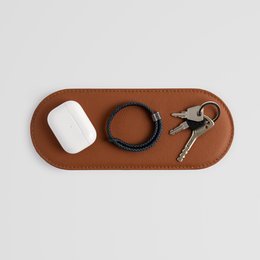 Stylish brown leather pad for small accessories. Available in black, brown, and grey. Decorative object with a rectangular shape and smooth leather surface.