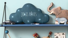 A blue linen cloud-shaped musical nightlight with the text "Jolly dreams" on it, surrounded by various baby toys and decor items on a shelf.