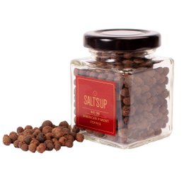 A glass jar containing whole Jamaican piment peppers. The jar has a red label and the peppers are dark brown in color.