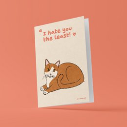 A greeting card featuring a cute cat illustration with the text "I hate you the least" printed on it. The card is in a love/romance category, with a playful and humorous tone.