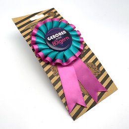 Colorful, striped buttons with text "Geboren in den 50er" and "Geboren in den 60er" indicating decade of birth. Circular award ribbons in vibrant pink and orange colors.