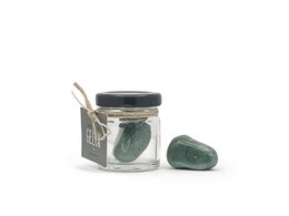 A small glass jar containing green aventurine crystals, a type of quartz known for its calming and grounding properties. The jar has a black lid and is surrounded by the natural crystals.