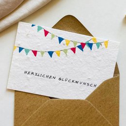 Plantable greeting card with colorful bunting garland, white textured paper, kraft envelope, German text "Herzlichen Glückwunsch"