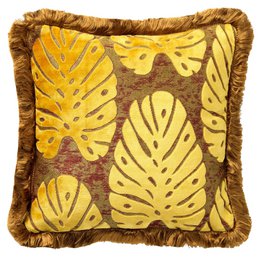 A square throw pillow with a golden yellow color and a tropical leaf pattern. The pillow has a plush, textured surface and a decorative fringe trim.