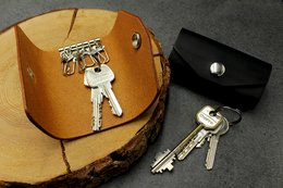 Leather key case/wallet in cognac and black colors, featuring a snap closure and metal hardware for secure storage of keys.