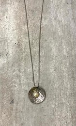 A long silver necklace with a round pendant featuring a shimmering crystal-like design.