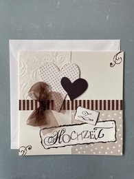 Folded wedding card with envelope. Embossed design featuring a heart-shaped element and decorative ribbon. Neutral color palette with touches of brown and black.