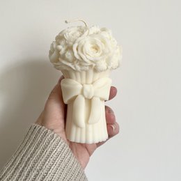  Cream, beige, and pastel-colored pillar candle with a bouquet of white roses on top.
