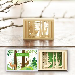 A small wooden box with a silhouette of a forest scene, including trees, deer, and other wildlife. The box is available in multiple languages, including German, English, French, and Dutch.
The product appears to be a decorative wooden box or frame featuring a laser-cut silhouette design of a forest scene. The design includes trees, deer, and other wildlife elements. The product is available in multiple language variants, indicating it may be marketed for an international audience.