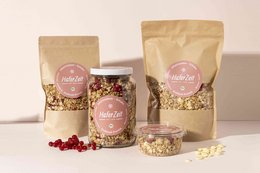 Organic currant-chocolate granola in paper bags and glass jar. Granola contains oats, currants, chocolate, and other natural ingredients. Available in 750g and 300g sizes.