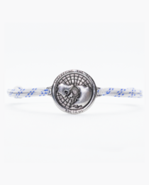A delicate silver charm bracelet with a circular charm featuring a detailed footprint design, set against a wooden background.