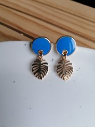 Blue statement earrings with gold-tone monstera leaf charms.
