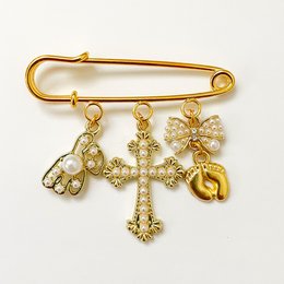 A gold-colored pin with a cross charm and other dangling charms, including a horseshoe, a four-leaf clover, and a crescent moon. The pin appears to be a lucky charm or christening gift.