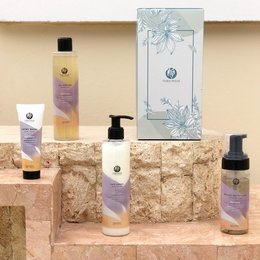 A set of natural beauty products featuring lavender, orange, and other botanical elements. The products include a bottle, tube, and spray bottle with floral and nature-inspired packaging.