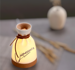 Small, round, ceramic essential oil diffuser with amber-colored glass body and white ceramic top. Features the word "Vapessence" printed on the glass.