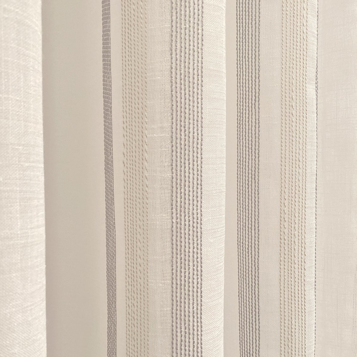 Cortina translúcida de color gris confeccionada en ollados. Visillo Jacquard de rayons verticaux fabriqué avec des matériaux recyclés et de qualité. Couleurs naturelles et calidos. Cortines pour salon, dortoir et cuisine.