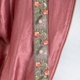 Pink shoulder bag with floral embroidered strap, made of soft, textured material.