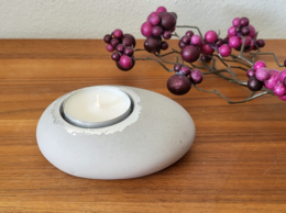 Grey ceramic tea light holder with purple berries on wooden surface.