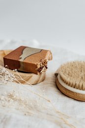 Handmade natural soap with earthy colors and textures, featuring a bar of soap and a wooden brush on a rustic wooden surface.
